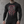 A tattooed man stands against concrete in the black shirt, the red skull and sword print on the chest