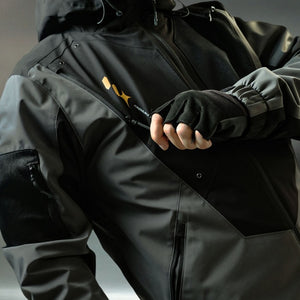 Gloved hand opening the chest zip pocket of the grey techwear windbreaker, snap studs in focus