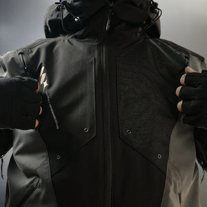 Both hands holding the jacket open: two black loop-field panels, printed lettering, snap studs