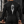 A muscular man in a locker room wears the black compression shirt, back view with the large spiked C print