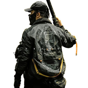 Person wearing a black tactical jacket with logos, holding a weapon on a white background
