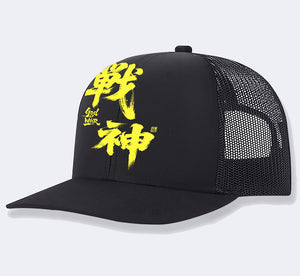 Black trucker hat with a bright yellow kanji print and black mesh back, three-quarter side view