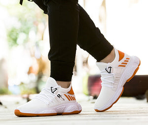 White knit mesh sneakers with orange stripes worn with black joggers, walking outdoors