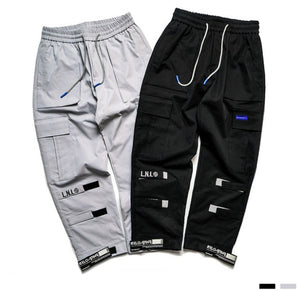 Label Patch Techwear Cargo Pants szürke-fekete színben lapra fektetve, combzsebek, szalagfülek a térd alatt és a bokánál