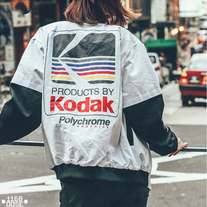 Second back view of the white baseball bomber jacket in the street, showing the ribbed black hem