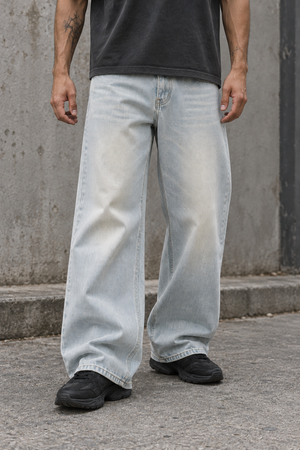 Cropped front view of the light wash baggy jeans worn with a dark tee, wide legs stacking over sneakers