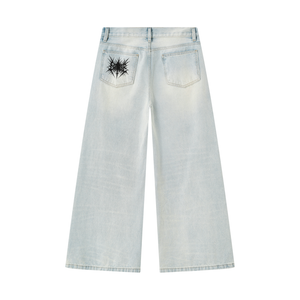 Back of the light wash baggy jeans laid flat, a black spiked emblem on the left back pocket and wide legs