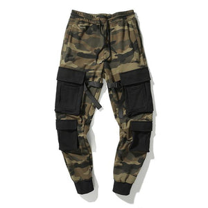 Loaded Pocket Camo Cargo Pants laid flat, camouflage with big black patch pockets, a buckled strap and ribbed cuffs