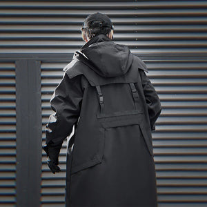 Person wearing a long black coat standing in front of a corrugated metal wall.