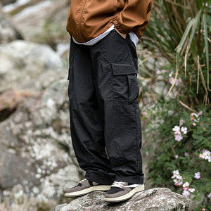 Loose Nylon Cargo Pants in black, model standing by rocks, flap cargo pocket on the thigh and wide straight leg