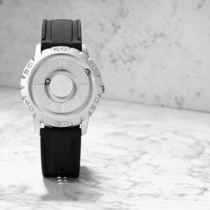 Silver-colored magnetic watch standing on a marble surface, front view of the light dial and notched bezel