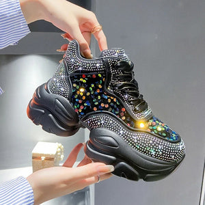 Black sneakers with colorful rhinestone details held by a person against a neutral background