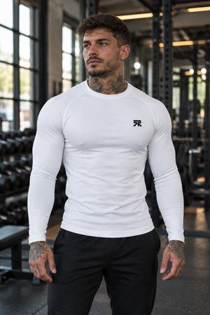 A man stands in a gym in the white compression shirt with black trousers, the small chest logo