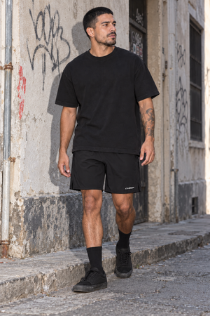 Model walking in a graffiti alley in the Black nylon athletic shorts and a black tee, front three-quarter view