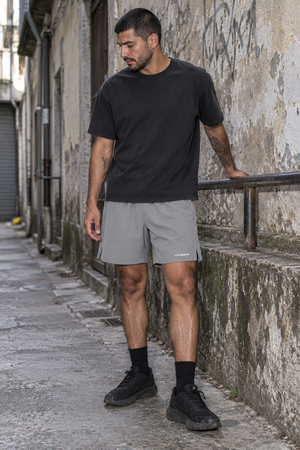 Model in the Light Gray athletic shorts and a black tee resting a hand on a railing in a narrow street