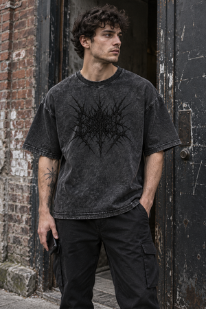 Man in the Black oversized acid wash tee by a brick doorway, front view with the dark thorn graphic