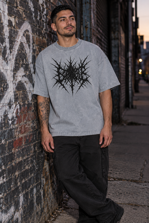 Man leaning on a graffiti wall in the Light Gray acid wash tee, front view with the black spiky print