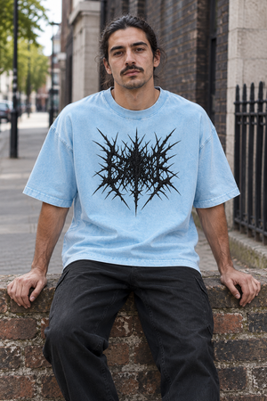 Man sitting on a low wall in the Sky Blue oversized acid wash tee, front view of the black thorn artwork