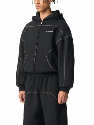Model in the zipped black boxy hoodie and matching sweatpants, front three-quarter view of the ribbed hem