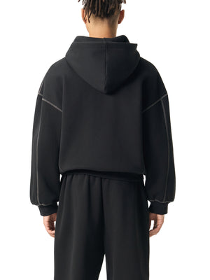 Back view of the oversized black hoodie on a model, hood down, grey seams running along the sleeves