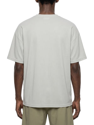 Mand i den lysegrå T-shirt med dropped shoulders set bagfra, afslappet kasseformet pasform over olivengrønne shorts