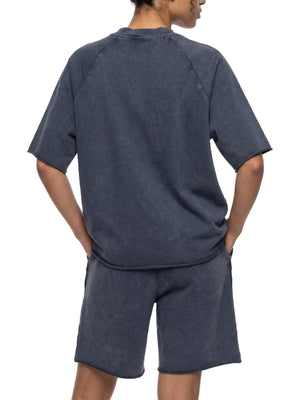 Kvinde set bagfra med hænderne bag sig i den marineblå raglan-t-shirt med mineralvask og shorts