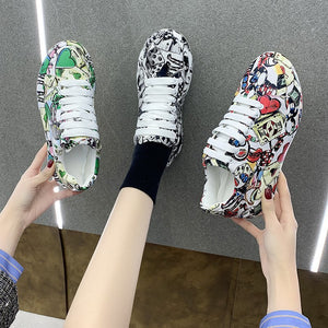 Hands holding Black and Green painted sneakers above a foot in a Red pair, view from above