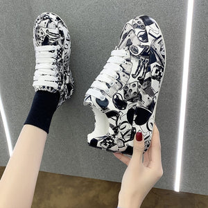 Black and white cartoon print platform sneakers held and worn, top view on a grey floor