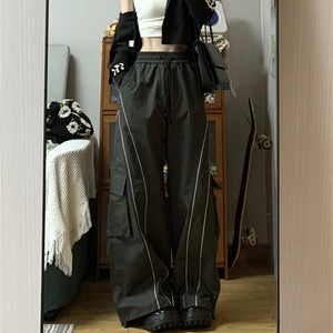 Parachute Track Y2K Pants in charcoal gray worn with a cropped black jacket, wide legs and curved light piping