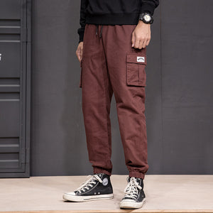 Brown patch pocket cargo joggers in front view, white label on the thigh pocket and black canvas high-tops
