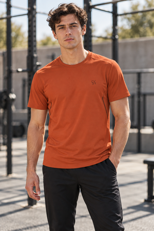 Orange workout t-shirt on a man in an outdoor gym, front view with crew neck and small chest logo
