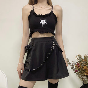 Modelo usando a saia cargo plissada preta com tira de corrente de ilhoses e bolso cargo, com top cropped preto com babados