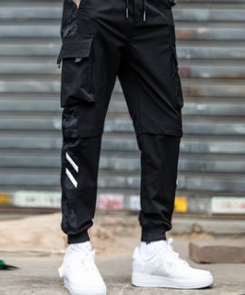 Black Reflective Stripe Techwear Joggers worn in front view, drawstring waist, cargo pockets and white sneakers