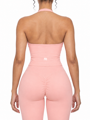 Back of the pink ruched halter top on a model, open back with a halter strap and a small logo low on the back
