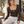 Model seated on a cafe bench in the Coffee bodysuit, holding a cup, scoop neckline and long fitted sleeves