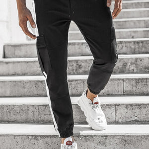 Black Side Stripe Techwear Joggers worn by a man on stone steps, front view with flap pockets and white sneakers