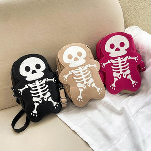 Schwarze, beige und Hot-Pink-Skelett-Taschen nebeneinander auf einem Sofa, jeweils mit weißem Totenkopf-und-Knochen-Design