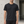 Man in the Black Slim Fit Athletic T Shirt, front view by a concrete wall, small logo near the hem