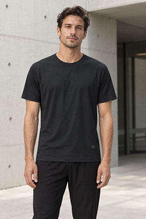 Man in the Black Slim Fit Athletic T Shirt, front view by a concrete wall, small logo near the hem