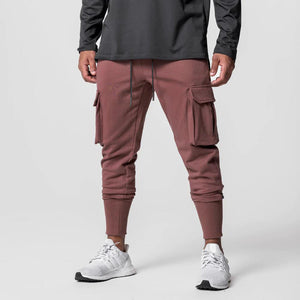 Rust Red Slim Fit Techwear Joggers worn by a man, front view with flap cargo pockets, ribbed cuffs and white shoes