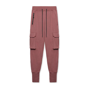 Rust Red tapered cargo joggers shown flat, front view of the black drawstring, vertical zip and flap side pockets