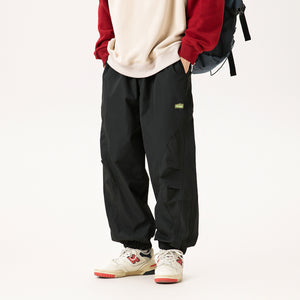 Man wearing the Straight Leg Cyberpunk Pants in black with a backpack, front view, patch label and cuffs