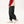 Black relaxed pants in side view while walking, red sleeve hoodie, pleated knee and elastic cuffs