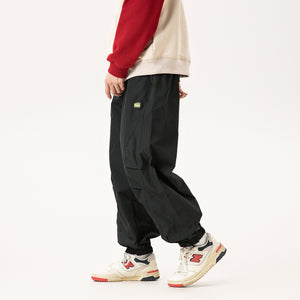 Black relaxed pants in side view while walking, red sleeve hoodie, pleated knee and elastic cuffs