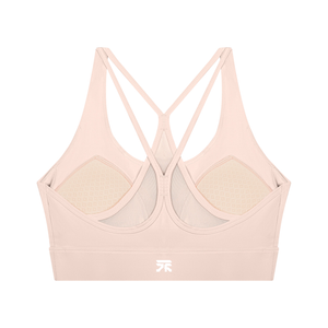 Back of the light pink sports bra laid flat, star cross straps and the pads visible inside the cups