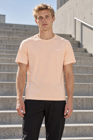 Man in the Light Pink Stretch Athletic T Shirt, front view on outdoor steps, small chest wordmark
