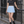 Model leaning on a black railing in the Sky Blue pleated tennis skirt, front view with a grey crop tee