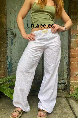 White eyelet embroidered wide leg pants worn with a green tank top, full front view in a doorway
