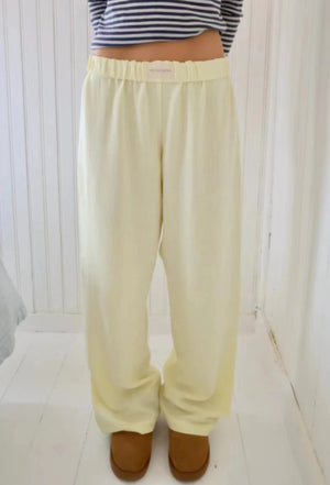 Pale butter yellow wide leg pants with an elastic waistband, front view on a wooden floor