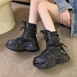 Model seated wearing the Tech Wear Boots Black, side view of the high platform sole and buckled strap